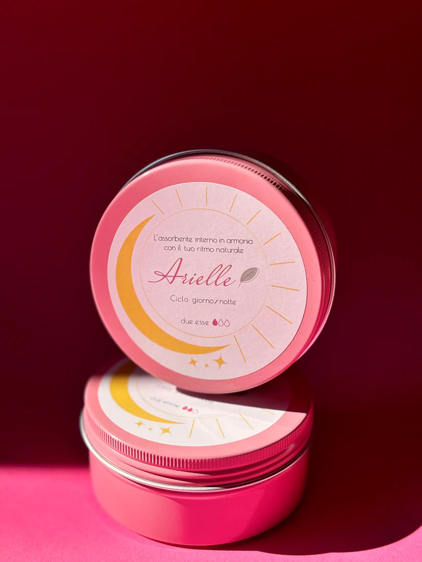 Spugna mestruale Arielle in spugna naturale con anello, accanto al barattolo rosa del prodotto con un mucchio di percarbonato,su sfondo rosa e bollino taglia s