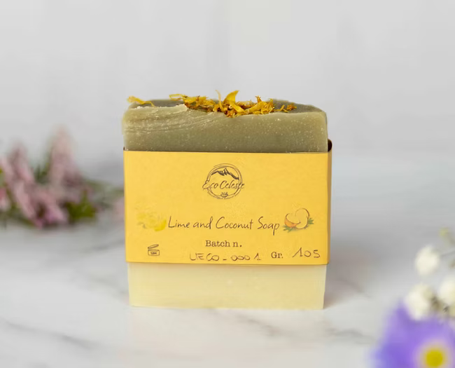 ECO-CELESTE: Sapone Cocco e Lime per il corpo. panetto tagliato a mano forma rettangolare. bianco e verde con petali gialli in cima. etichetta gialla in carta con critta del brand e nome prodotto