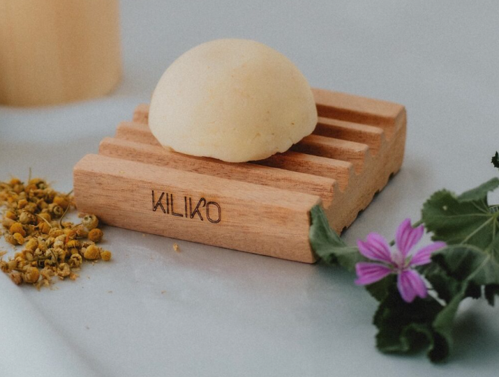 detergente intimo kiliko ph 5.3 adatto a tutta la famigilia.nella foto è appoggiato su un porta sapone in legno marchiato kiliko. il detergente è solido di colore chiaro che vira al color crema