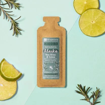 Ricarica deodorante “Biodeo Alaska Tea Tree e lime" di La Saponaria su sfondo rosa, circondata da fette di lime e rametti di salvia.
