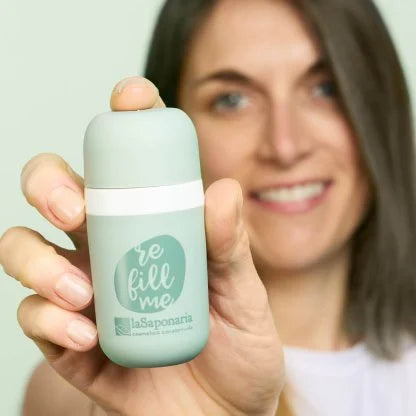 Donna che sorride mentre tiene in primo piano un applicatore roll-on riutilizzabile verde “Refill Me” del marchio La Saponaria.